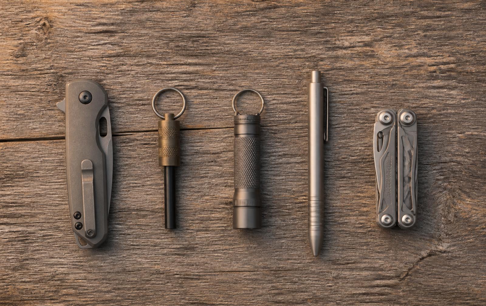 Pocket knife, keychain firesteel, keychain light, pen and mini multi-tool on wood